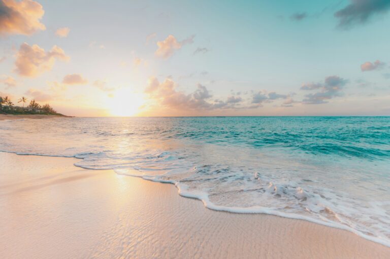Ocean waves washing onto a white-sand beach with the sun setting in the background.