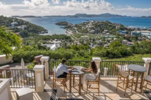 a couple sitting at a table enjoying drinks as they look over Cruz Bay at The Hills St John in the USVI.