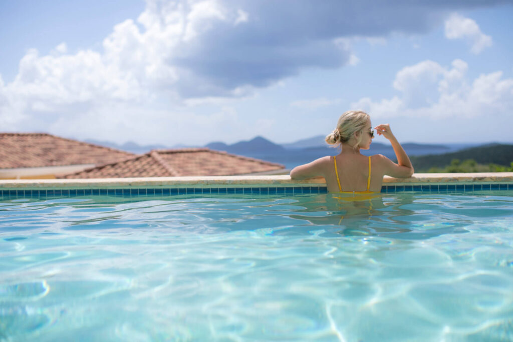 a woman relaxing in the water, at the edge of her villa's private pool that overlooks Cruz Bay in St John, USVI.