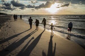 A family walking down the beach with the sunset in front of them.